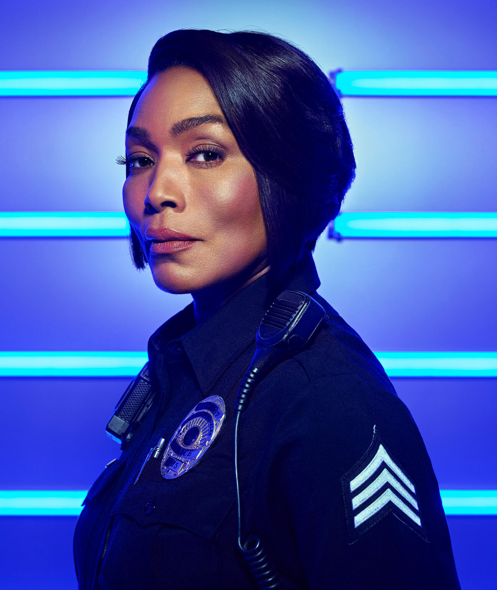 Angela Bassett as Athena wearing a straight bob and her police uniform in front of a blue neon light background.